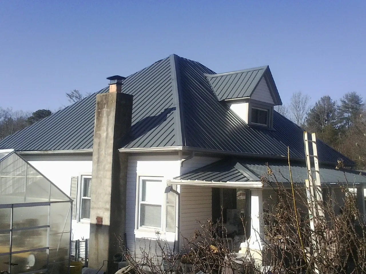Dark blue standing seam metal roof on a white farmhouse with dormer — Slate & Tile Roof Repair by Roofing Brothers in Calera