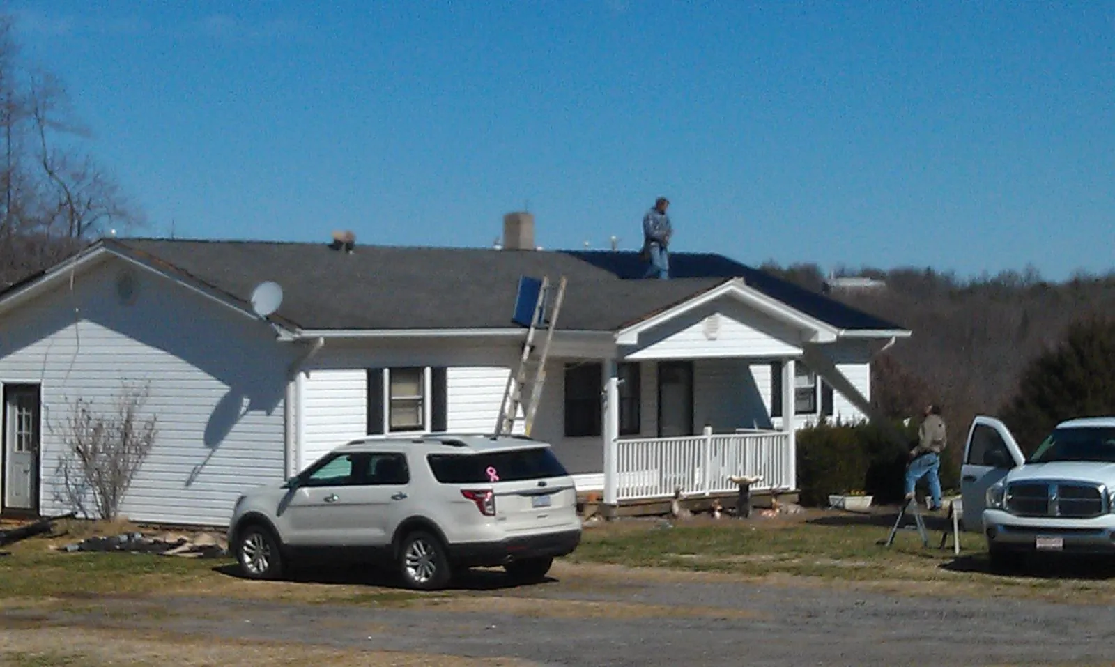 Roofers stripping shingles from a white ranch house roof in Calera