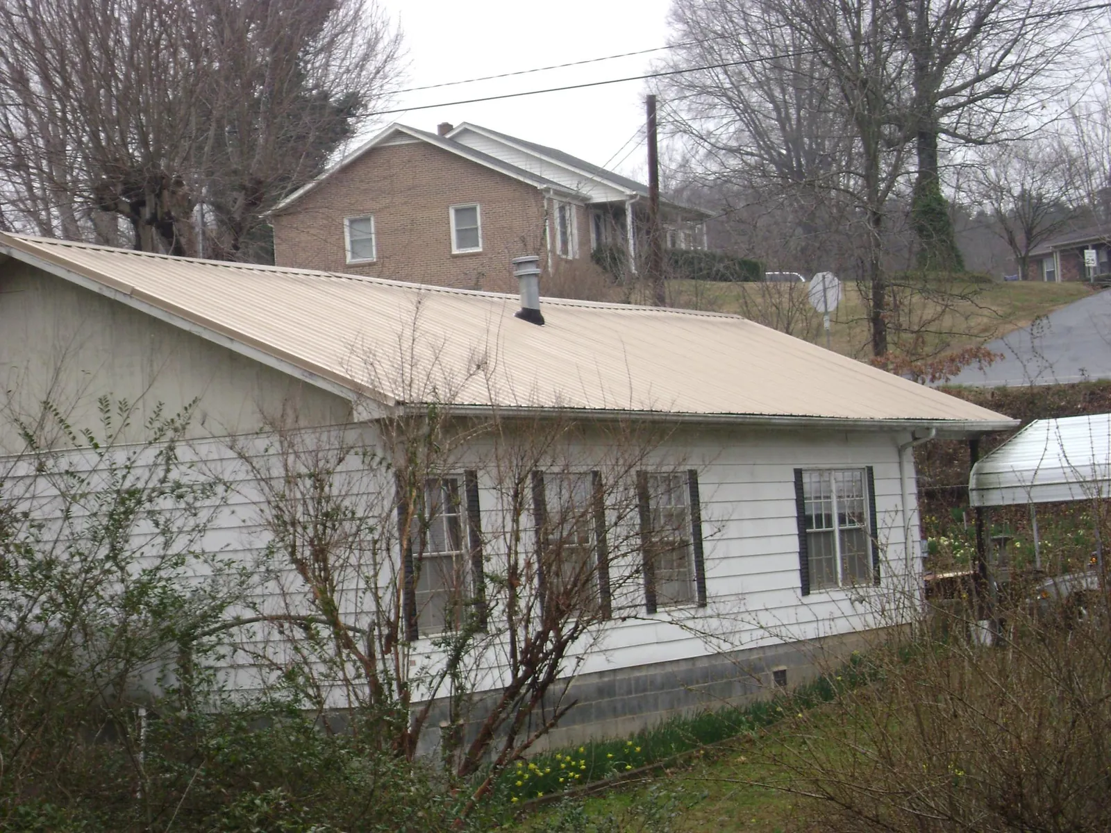 Tan metal roof on a white sided house set into a hillside — Commercial Roofing by Roofing Brothers in Calera